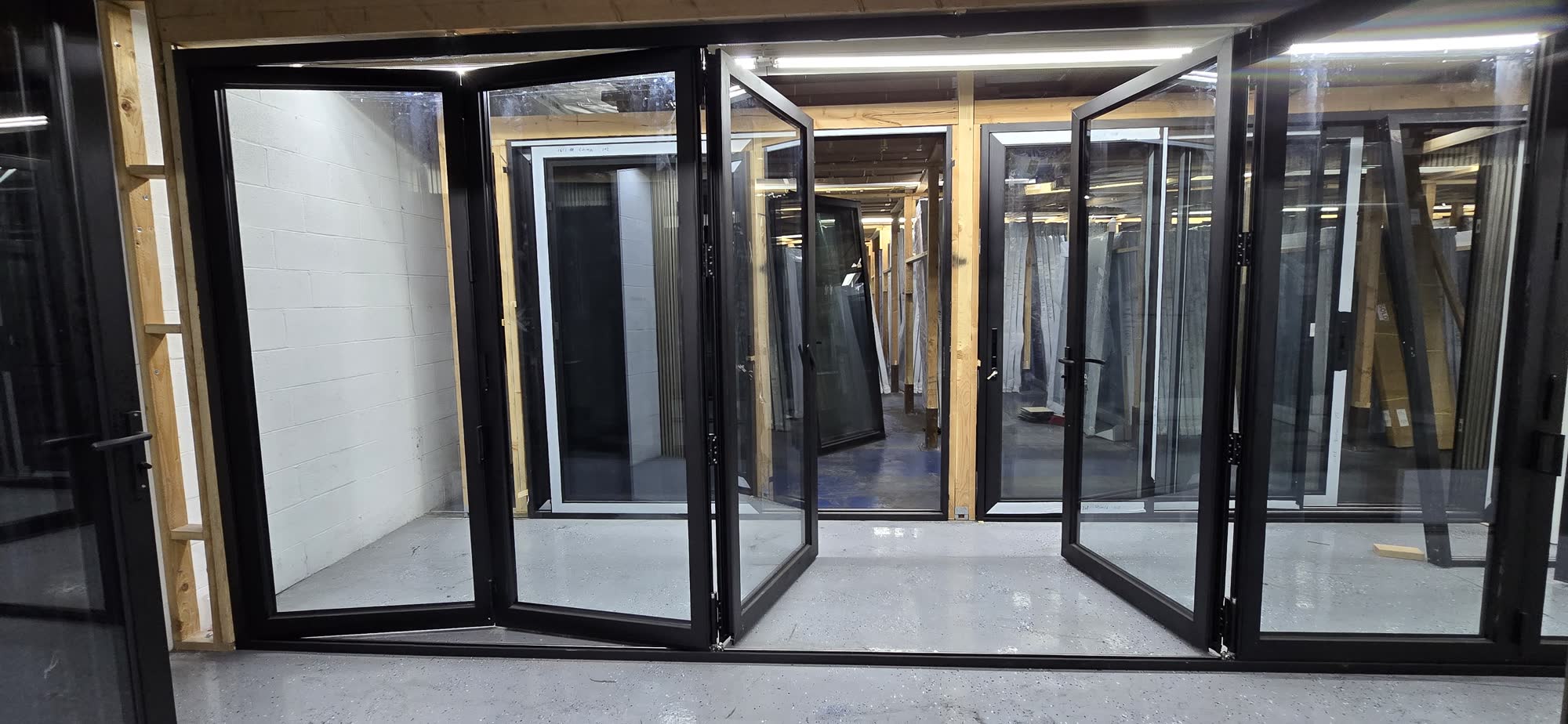Wide black aluminum bi-fold door system folded open in our fabrication facility
